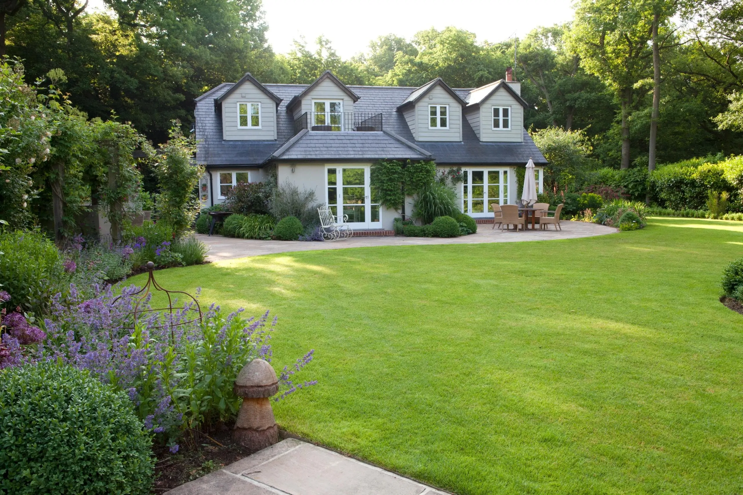 Expansive Surrey garden with manicured lawn, flowering perennial borders, and a contemporary country house in the background, exemplifying high-end bespoke garden design