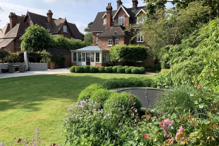 Historic house with formal lawn, topiary shrubs, and landscaped garden beds filled with flowering plants.