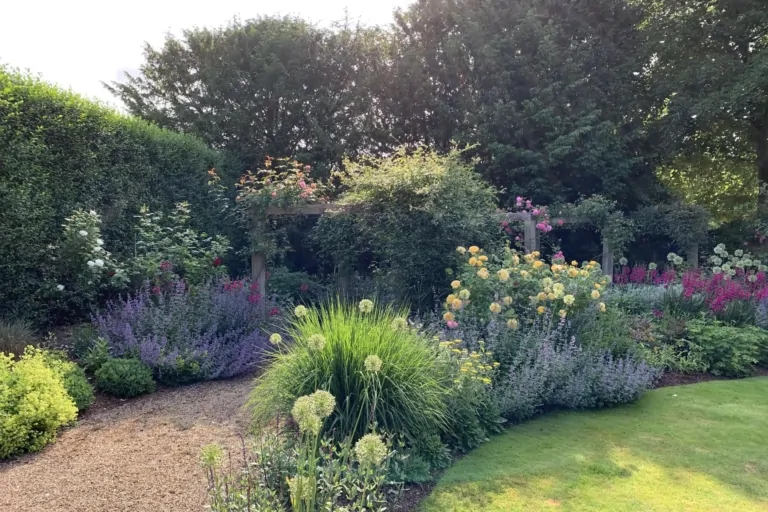 Curved garden border with flowering perennials, ornamental grasses, and manicured lawn creating a lush landscape.