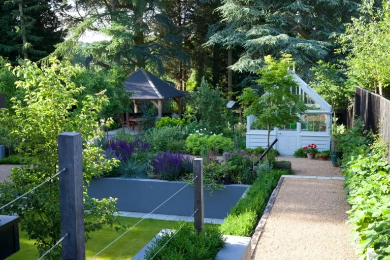 Lush garden with manicured paths, raised planters, small greenhouse, and diverse plants creating a serene outdoor space.