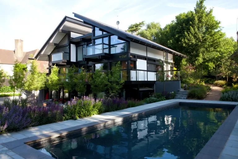 Contemporary house with black-and-white exterior overlooking a modern backyard pool surrounded by greenery and purple flowering plants.