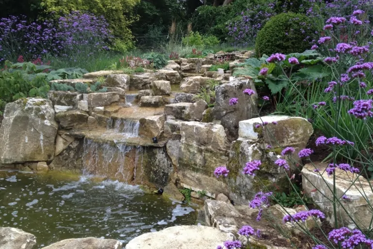 Rock waterfall surrounded by purple flowering plants creating a natural focal point in a landscaped garden.