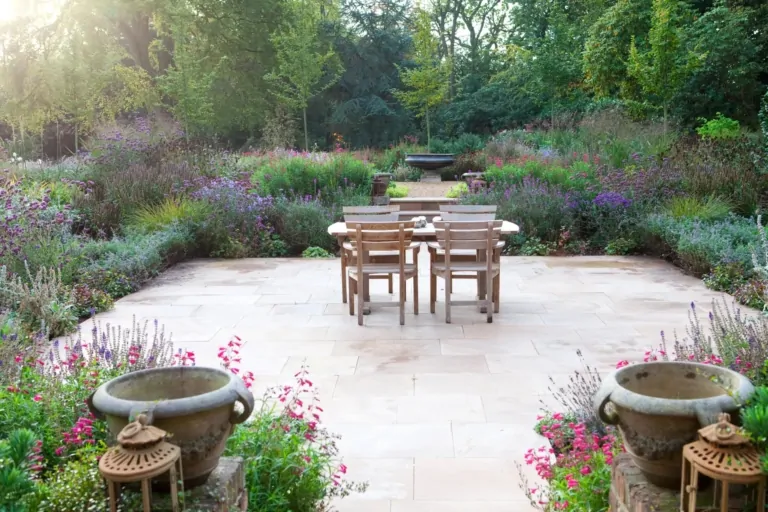 Garden terrace framed by dense, flowering borders and ornamental stone planters, offering an inviting outdoor space in a bespoke Surrey garden.