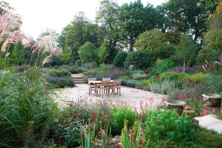 Outdoor patio with wooden dining furniture surrounded by diverse perennial planting, illustrating a carefully curated luxury garden environment.