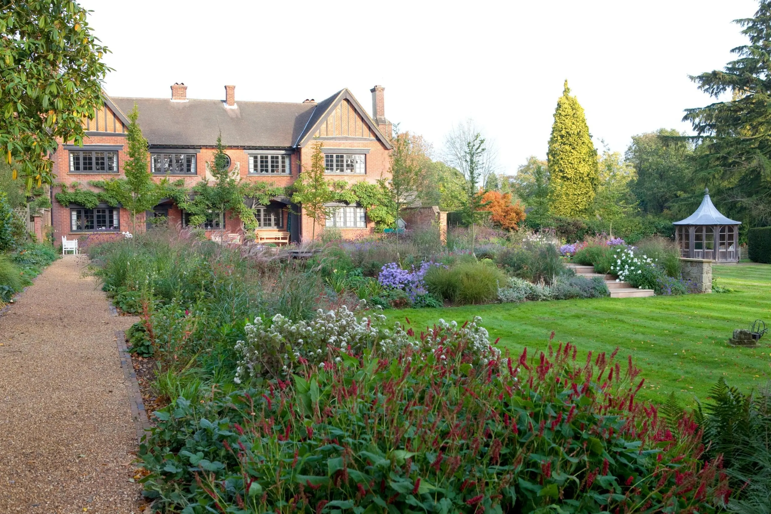 Elegant Surrey garden with lush perennial borders, manicured lawn, and traditional brick country house in the background, designed by We Love Plants.
