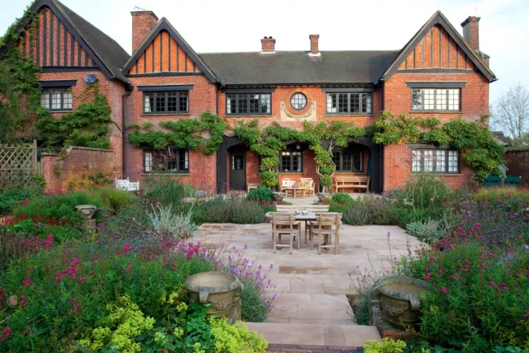 Formal garden patio with seating area surrounded by colorful flowering plants and climbing greenery on a red brick Surrey home, showcasing bespoke garden design.