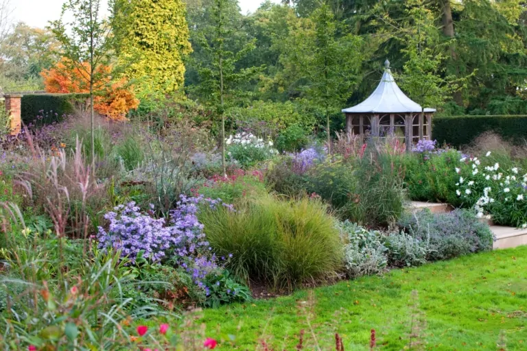 Ornamental gazebo and curved planting beds with seasonal flowers in a luxury garden setting, featuring structured landscaping and soft foliage.