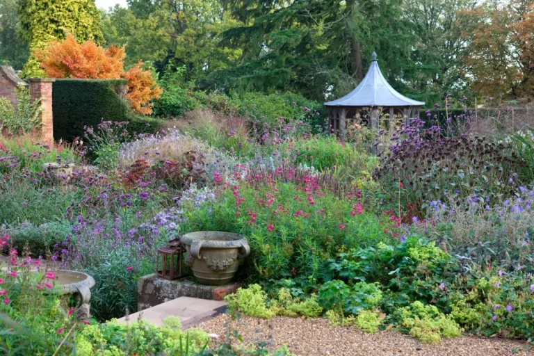 Serene garden view with layered perennial plantings, lush greenery, and decorative urns, highlighting naturalistic planting design by We Love Plants.