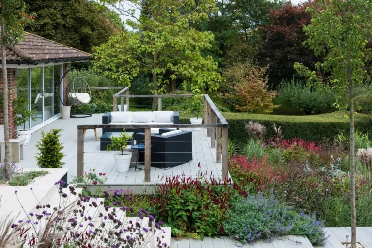 Luxury modern Surrey terrace with grey seating, flowering perennials, and layered planting beds, exemplifying bespoke garden design.