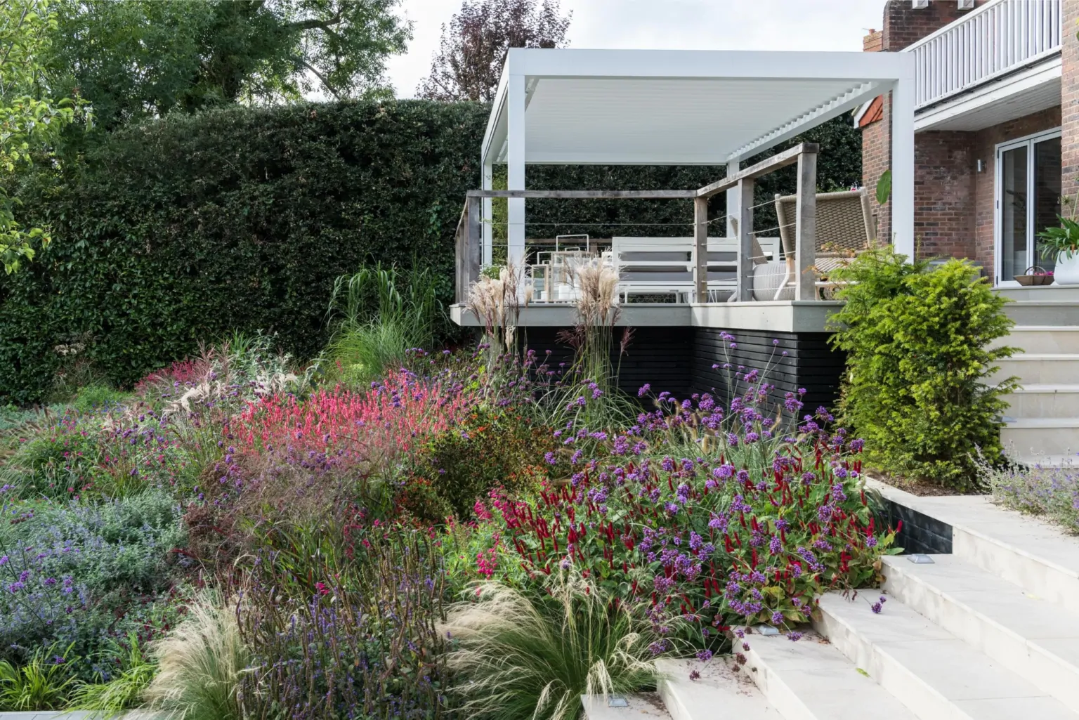 Modern outdoor terrace with white seating and vibrant mixed perennials, demonstrating high-end Kent garden landscaping.