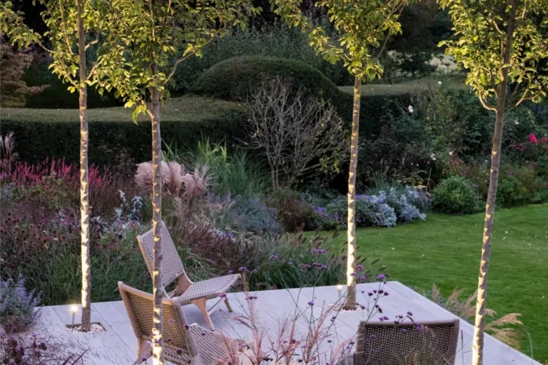 Contemporary Surrey garden terrace with layered perennial planting, seating area, and manicured greenery, highlighting structured luxury garden design.