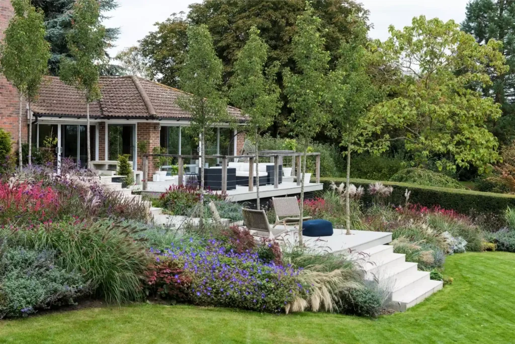 Terraced Surrey garden with manicured lawn, layered perennial planting, and contemporary outdoor seating, illustrating luxury garden design and bespoke landscaping by We Love Plants.
