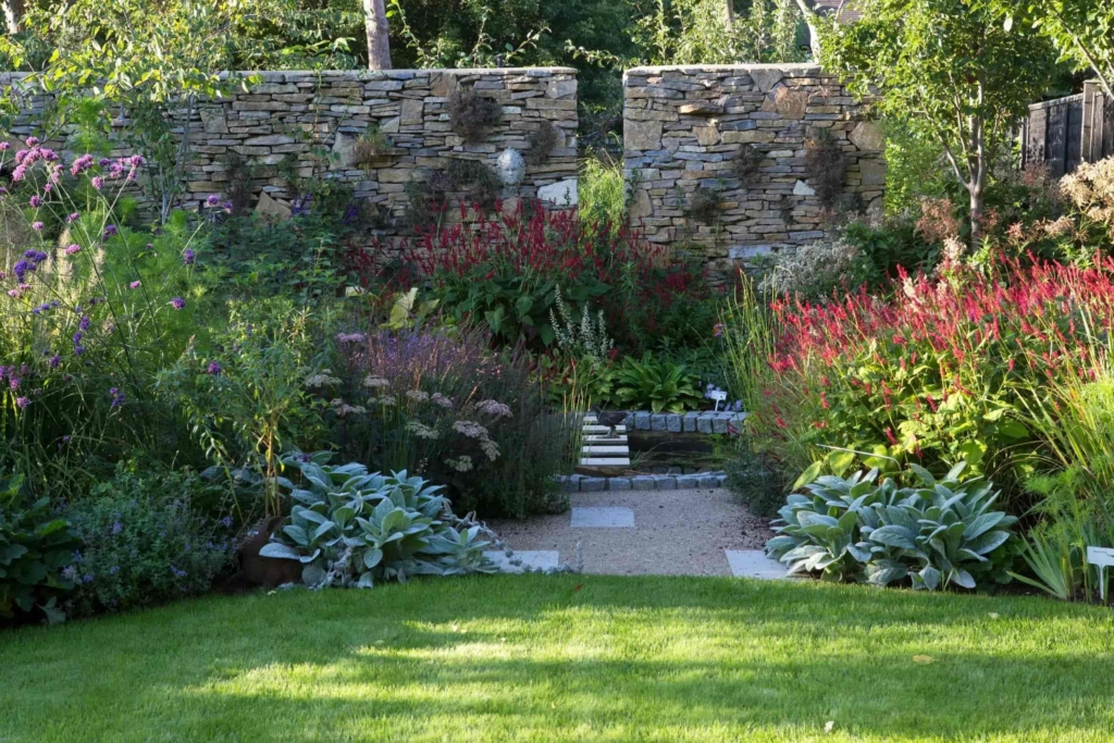 Formal Surrey garden with manicured lawn, layered perennial borders, and a textured stone wall, highlighting luxury and structured garden design