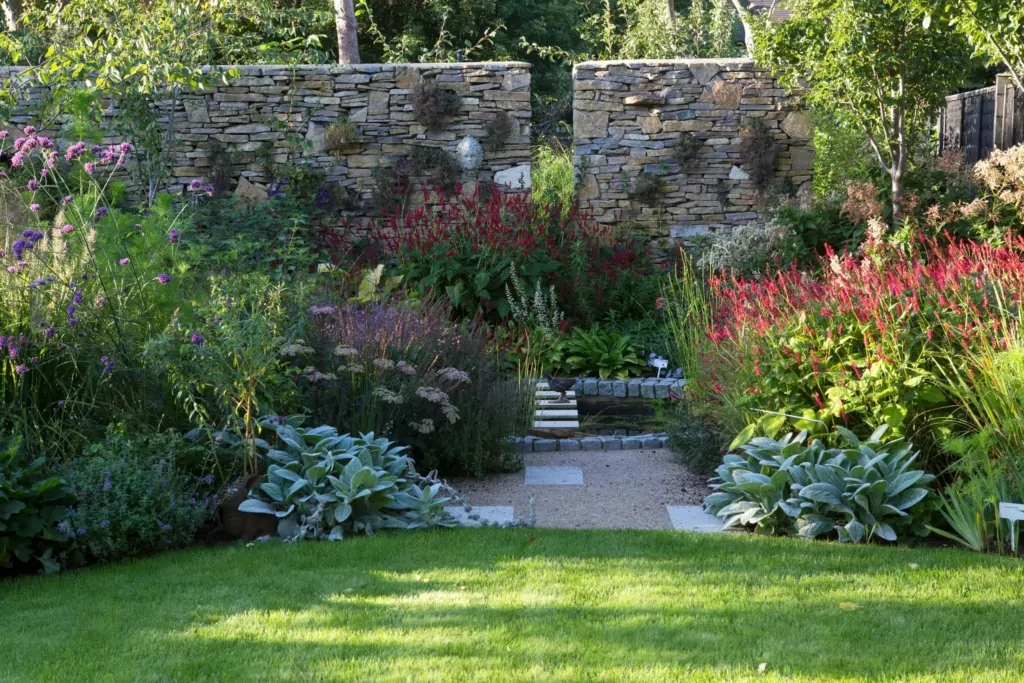 Formal Surrey garden with manicured lawn, layered perennial borders, and a textured stone wall, highlighting luxury and structured garden design