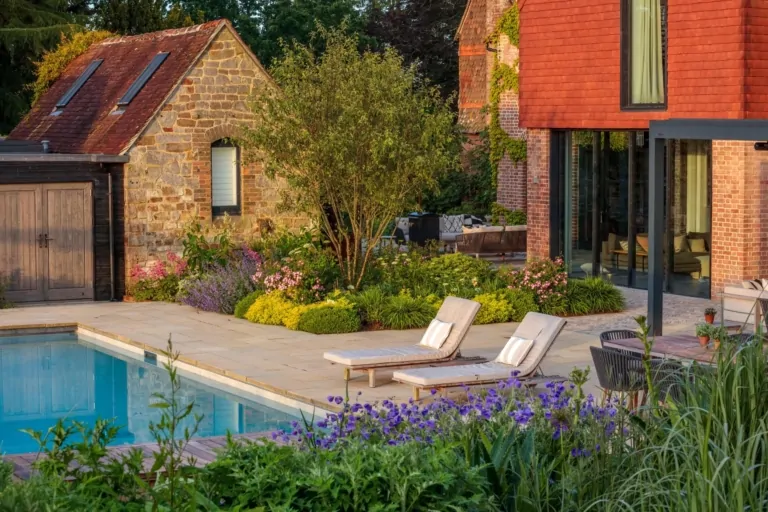 Poolside terrace with sun loungers, vibrant perennial planting, and modern architecture in the background, exemplifying luxury garden design.