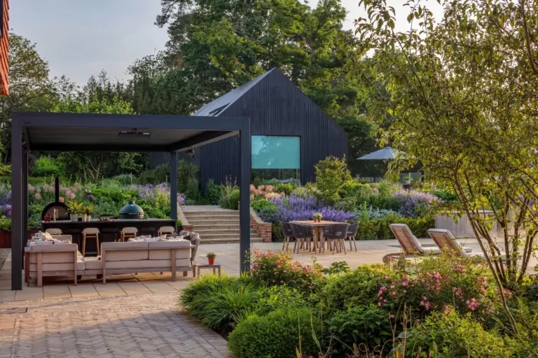 Outdoor dining and seating area surrounded by lush planting and manicured hedges, showing high-end contemporary garden design.