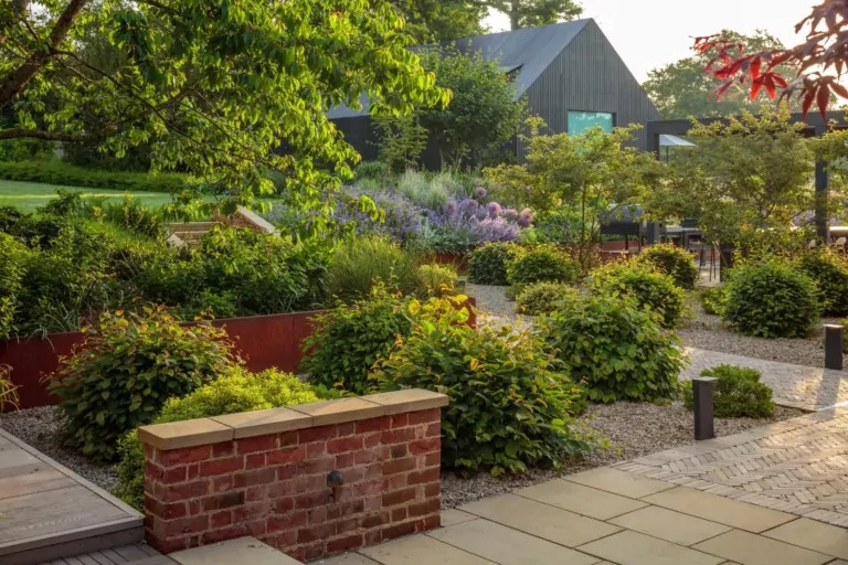 Terraced modern garden with manicured lawn, stone paths, and layered perennial planting, highlighting structured and luxury landscaping in Surrey.