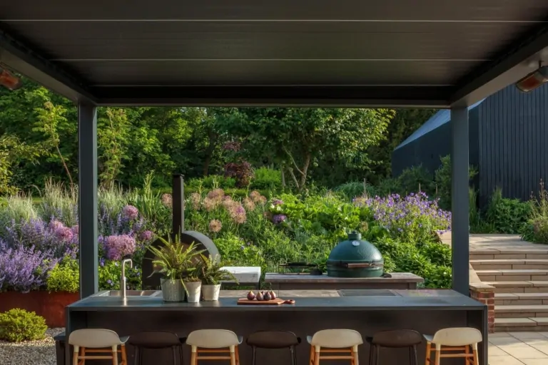 Outdoor kitchen and bar area in a modern Surrey garden with surrounding planting, terraces, and structured landscaping features.
