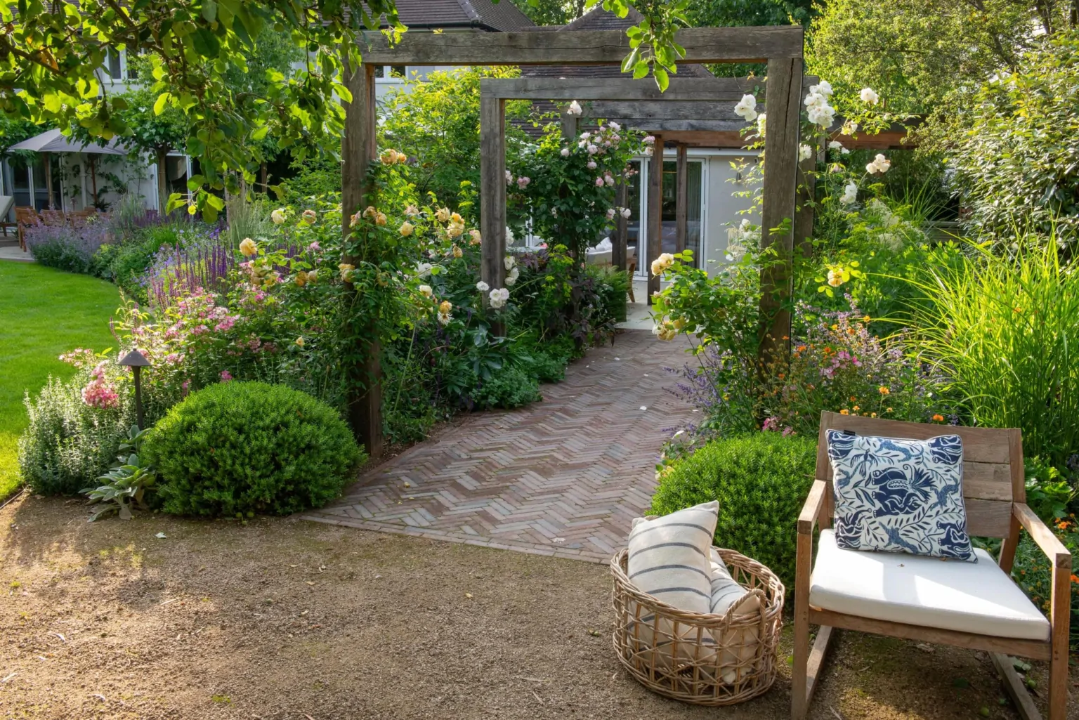 Shaded Surrey garden path with layered perennial planting, manicured shrubs, and outdoor seating, illustrating bespoke luxury garden design.