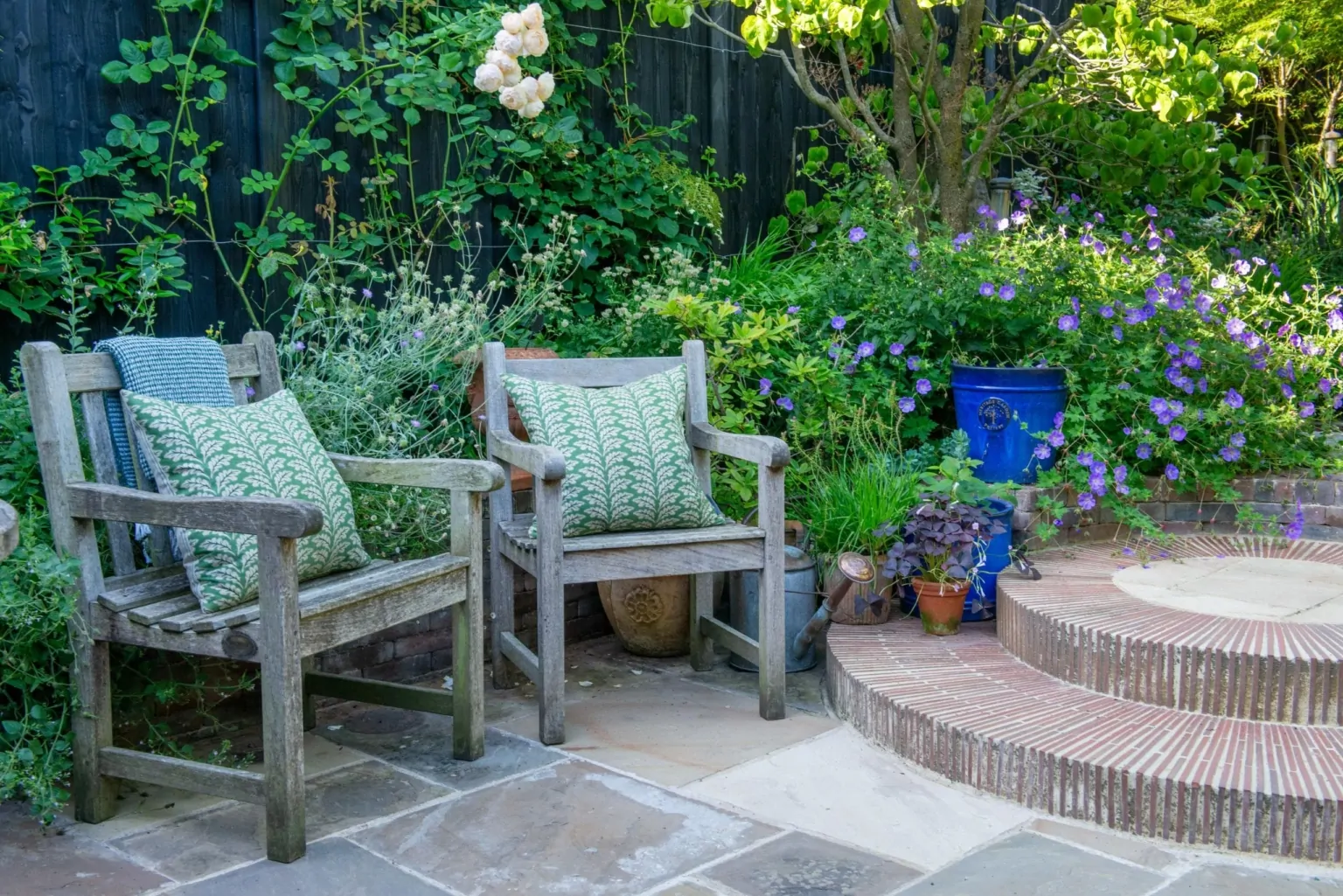 Outdoor seating area in a Surrey garden with layered perennial planting, manicured hedges, and structured pathways, exemplifying bespoke luxury design.