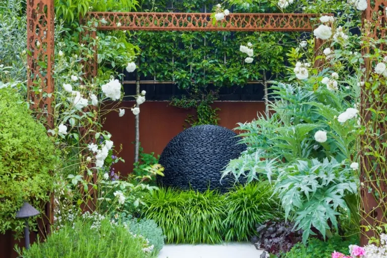 Decorative garden arch with white flowering plants and ornamental foliage creating a framed entrance in a landscaped garden.