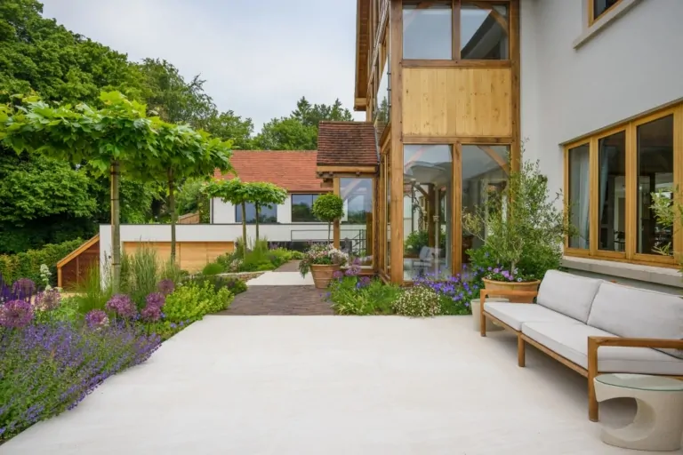 Modern outdoor patio with wooden bench and flowering plants, highlighting minimalistic and natural garden design.
