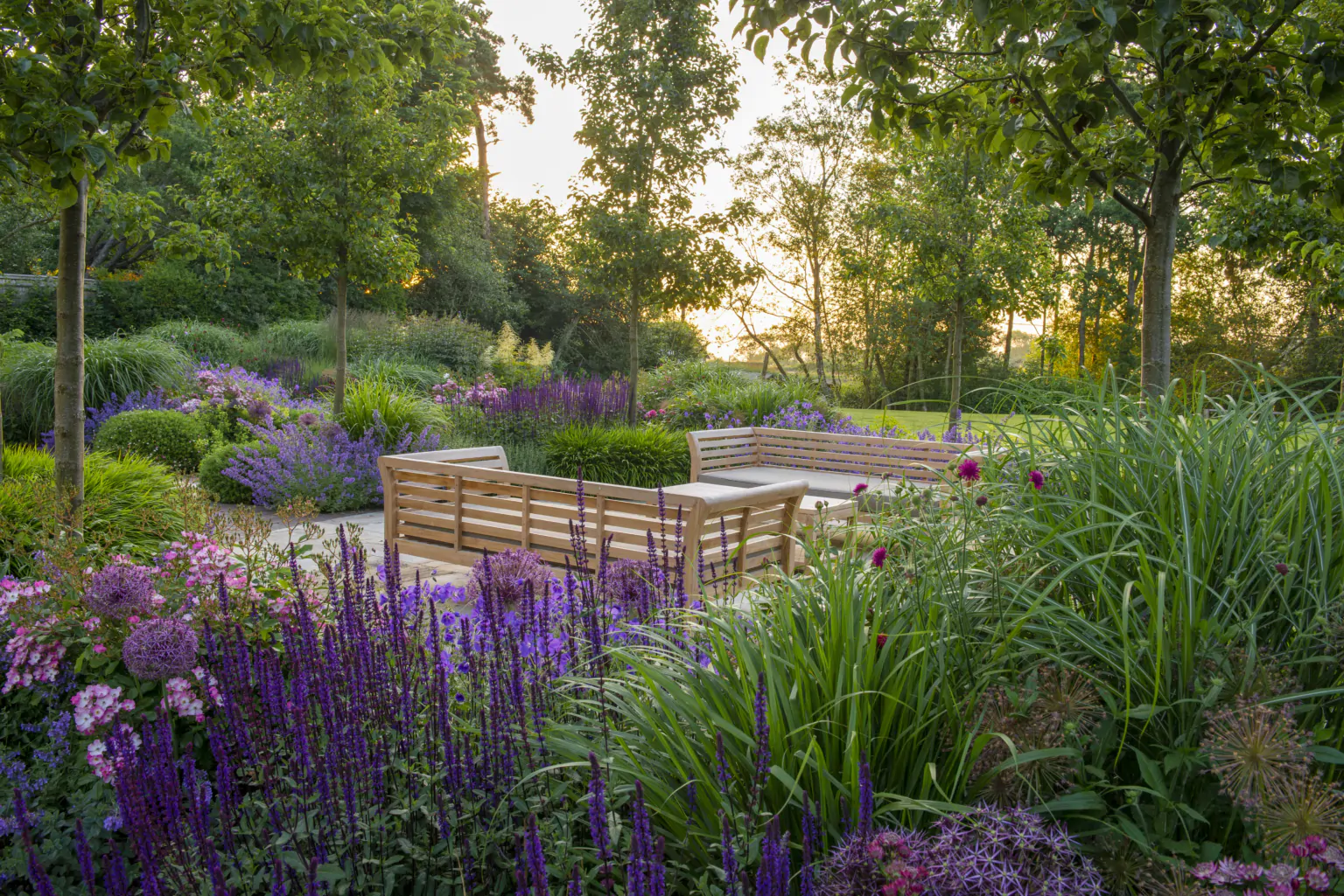 Formal garden with manicured lawn, flowering borders, ornamental grasses, and neatly trimmed hedges.